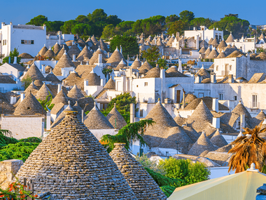 Panoramic view of Alberobello showing numerous white trulli houses with distinctive conical stone roofs scattered across the town.
