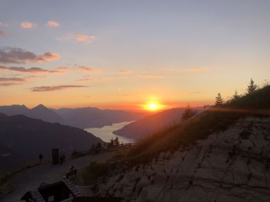 Von der Schynigen Platte sieht man hinunter auf dem See. Die Sonne küsst den Horizont und der Himmel erstrahlt in orangen Farben.