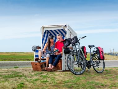 Der Nordsee entlang geht's weiter. Zwei Radfahrer sitzen in einem blau-weiß gestreiften Strandkorb mit ihren Tourenrädern in der Nähe auf einer Wiese an der Nordsee.