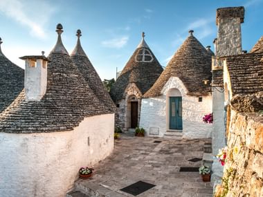 White trulli houses with distinctive conical stone roofs in Apulia. The traditional buildings feature white walls and blue doors.