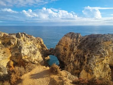 Goldene Kalksteinklippen mit natürlichem Felsbogen bei Ponte da Piedade, Algarve. Türkisfarbenes Meer und blauer Himmel mit weißen Wolken.