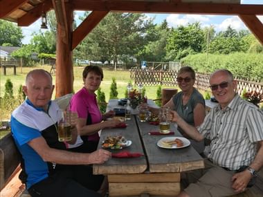 Vier Radfahrer sitzen am Holztisch unter rustikalem Pavillon während Mecklenburger Radtour und geniessen Mahlzeit mit Biergläsern und Tellern.