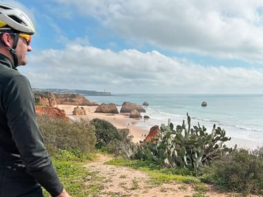 Radfahrer mit Helm und Sonnenbrille betrachtet Sandstrand mit Felsformationen an der portugiesischen Küste zwischen Porto und Lissabon.