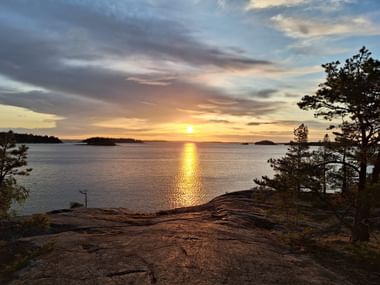 Blick von einer Erhöhung über das Meer in Mossala, Finnland. Im Hintergrund geht die Sonne unter.