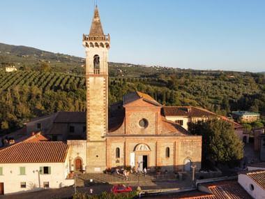 Der Geburtsort von Leonardo da Vinci. Steinkirche mit hohem Glockenturm in Vinci, Toskana, umgeben von Gebäuden mit Terrakottadächern und Hügeln mit Olivenhainen.