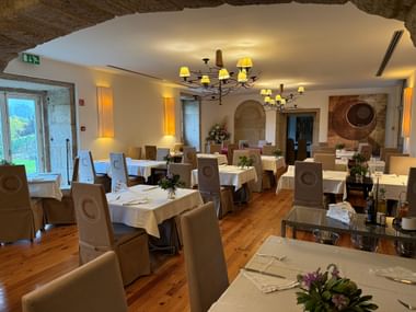 Eleganter Speisesaal mit weißen Tischdecken, beigen Stühlen, Holzboden, Steinbogendecke und Kronleuchtern im Hotel Convento dos Capuchos.