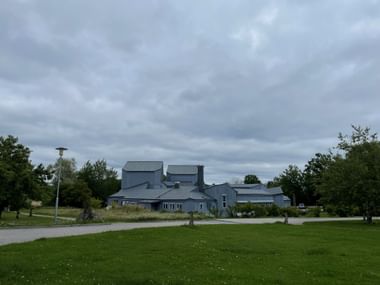 Moderner grauer Gebäudekomplex des Kulturhuset Ytterjärna mit markanten Metalldächern, umgeben von grünen Rasenflächen und Bäumen unter bewölktem Himmel.
