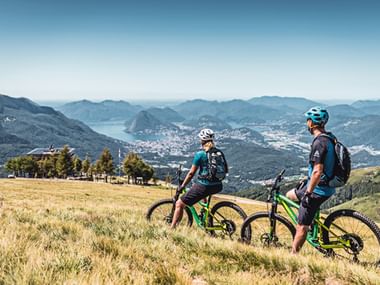 Zwei Mountainbiker machen in einem Feld eine Pause und schauen sich die wunderschöne Berglandschaft an.