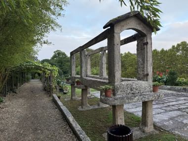 Traditioneller portugiesischer Hórreo-Getreidespeicher aus Granit mit Säulen und Lamellenwänden in einem Garten in Monção mit Bäumen und Blumen.
