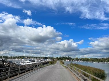 Gerade Straße mit Geländern zwischen zwei Yachthäfen mit Booten und Schilf unter blauem Himmel mit weißen Wolken bei Trosa.
