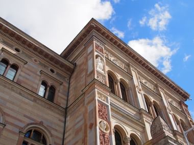 Aufwärtsblick auf verzierte historische Gebäudefassaden mit Bogenfenstern und dekorativen Elementen in Stockholms Altstadt vor blauem Himmel mit Wolken.