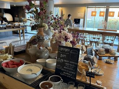 Frühstücksbuffet mit frischem Obst, Marmeladen, Gebäck und Blumendekoration in Vila do Conde. Eine Tafel zeigt hausgemachte Compota und Marmelade.