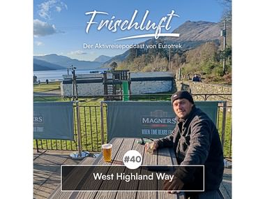 Mann auf Seeterrasse mit Bier, Berge im Hintergrund. Texteinblendung: Frischluft Podcast Folge 40, West Highland Way.