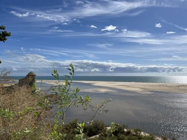 Küstenlandschaft bei Cacela Velha mit Wattflächen, Sandbänken und ruhigem Wasser unter blauem Himmel mit weißen Wolken.
