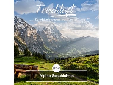 Alpine Berglandschaft mit grünen Wiesen und Holzbank. Texteinblendung: Frischluft - Der Aktivreisepodcast von Eurotrek, Folge 39 Alpine Geschichten.