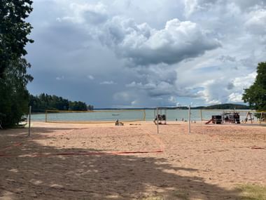 Ein Standstrand mit einem Beachvolleyballfeld und im Hintergrund das Meer und Laubbäume in Finnland.