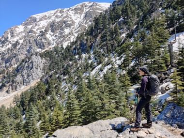 Frau steht vor Wald und Berge, die leicht vom Schnee bedeckt sind.