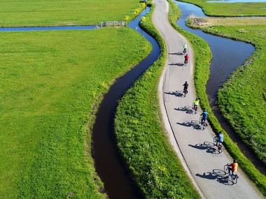 Vue aérienne de cyclistes roulant sur une piste cyclable sinueuse à travers le paysage vert de Hollande-du-Nord avec des canaux d'eau.