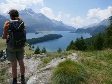 Eine Wanderin steht auf einer Anhöhung und blick auf einen Bergsee.