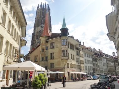 Mittelalterliche gotische Kathedrale mit hohem Turm dominiert einen Kopfsteinplatz in Freiburg, umgeben von traditionellen Schweizer Gebäuden.