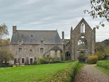 Abbaye de Beauport mit gotischer Kirchenruine und Steinwohngebäude. Ein Kiesweg führt durch grüne Rasenflächen zur Abteianlage.