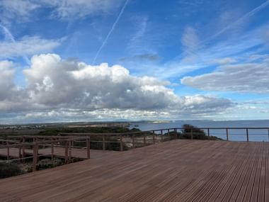 Holzaussichtsplattform mit Geländer mit Blick auf den Atlantik bei Sagres, Algarve. Blauer Himmel mit weißen Wolken über der Küste.