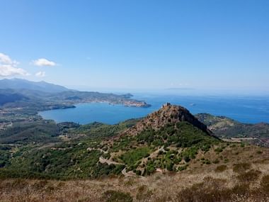 Atemberaubender Blick über die Insel Elba mit bewaldeten Hügeln, blauem Mittelmeer, Küstensiedlungen und einem markanten Felsgipfel.