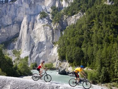 Zwei Mountainbiker auf der Naturstrasse vor der Felswand.
