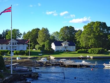 Front de mer pittoresque du fjord d'Oslo avec drapeau norvégien, maisons blanches parmi les arbres verts, marina avec bateaux et pontons.