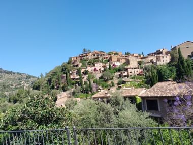Das Dorf Deià in Mallorca. Mehrere Steinhäuser umgeben von Bäumen befinden sich auf einem Hügel.