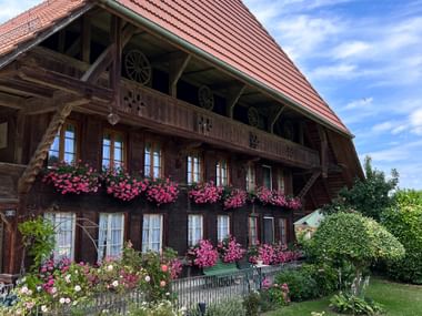 Ein traditionelles Holzbauernhaus mit roten Geranien an den Fenstern und einem blauen Himmel im Hintergrund.