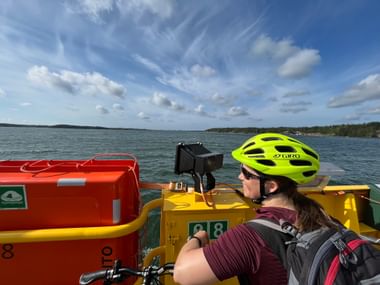 Eine Frau mit einem gelben Fahrradhelm fährt auf einer Fähre auf einem finnischen See