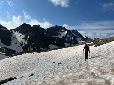 Ein Wanderer geht über ein Schneefeld mit Bergen im Hintergrund