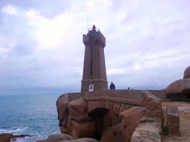 Leuchtturm Phare de Mean Ruz in Ploumanach an der Rosa Granitküste der Bretagne, aus rosa Granitblöcken mit Steinbrücke und großen Felsen.
