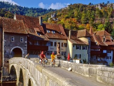 Zwei Velofahrer fahren über eine Brücke in St. Ursanne im Kanton Jura auf ihrer Velotour von Eurotrek von Basel nach Nyon.