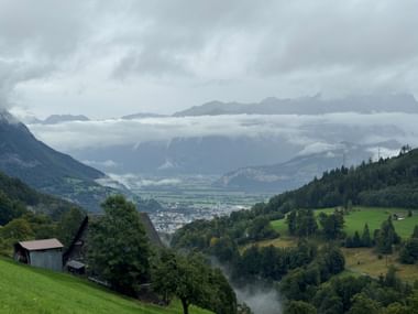 Alpentalblick bei Sargans mit grünen Wiesen, Wäldern und einer Stadt im Tal. Berge in tiefen Wolken unter bedecktem Himmel.
