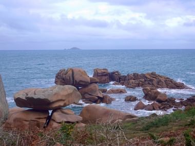 Rosa Granitfelsen an der Küste von Ploumanac'h, Bretagne. Runde Felsblöcke im blauen Meer verstreut mit Inseln am Horizont.