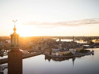 Luftaufnahme des Stockholmer Rathaus-Turms bei Sonnenuntergang mit der historischen Innenstadt und Wasserwegen im goldenen Licht.
