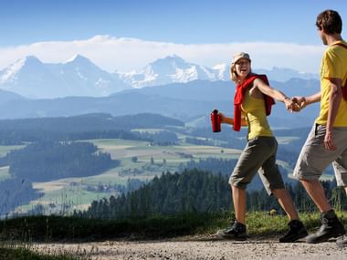A couple hiking in Moosegg in the canton of Bern on the Trans Swiss Trail with mountains in the background.