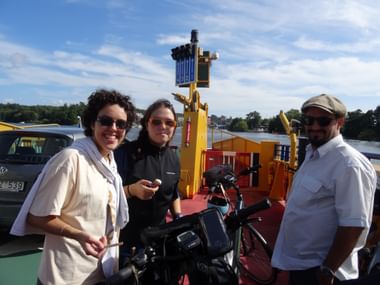 Drei Radfahrer mit Fahrrädern auf dem Deck einer gelben Fähre. Blauer Himmel und Wasser im Hintergrund bei Stockholm.