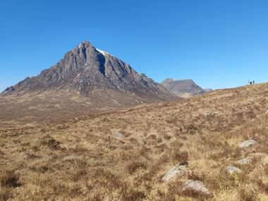 Berg Buachaille Etive Mor erhebt sich über Moorland mit goldenem Gras unter klarem blauen Himmel am West Highland Way in Schottland.