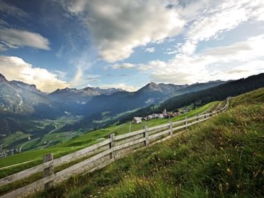 Schweizer Alpental mit Holzzaun Holzzaun auf grasigem Hang mit Blick auf Schweizer Alpental mit Bergen, Dörfern und dramatischem bewölktem Himmel.