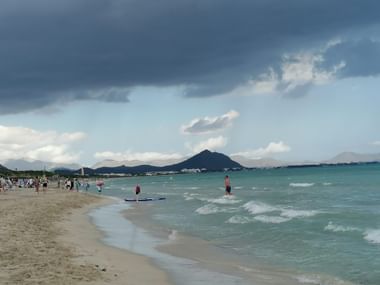 Strand und welliges Meer in Mallorca. Einige Personen sind am Strand. Der Himmel ist bewölkt.