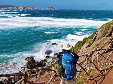 Ein Wanderer sitzt auf einem Felsenabschnit am Küstenweg auf Menorca.