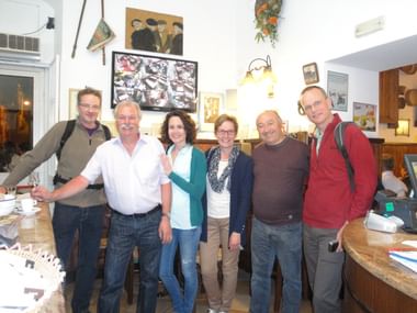 Gruppenfoto auf Sizilien mit Eurotrek-Reisenden Sechs Personen posieren zusammen in einem gemütlichen Restaurant-Interieur auf Sizilien. Die Gruppe besteht aus Männern und Frauen verschiedenen Alters.