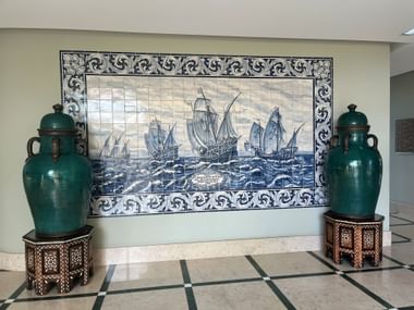 Portugiesisches Azulejo-Fliesenbild mit Segelschiffen, flankiert von zwei großen grünen Keramikvasen auf verzierten Holzständern in Alvor.