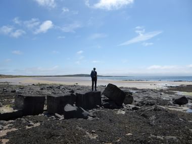 Wanderer auf einem Stein. Er betrachtet das Meer. Küstenwandern in Schottland. Wanderferien mit Eurotrek.