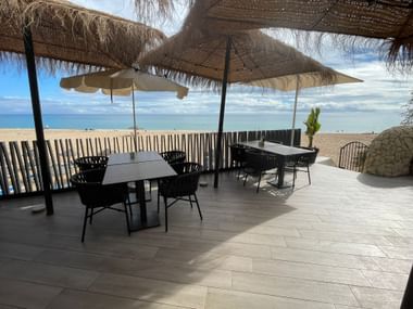 Strandterrasse des Restaurant Atlantico in Salema mit schwarzen Tischen und Stühlen unter Strohschirmen mit Blick auf den Atlantik.