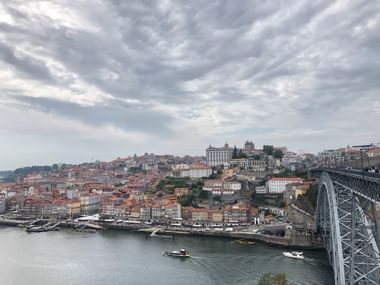 Panoramablick auf Portos historischen Hang mit Gebäuden mit Terrakottadächern entlang des Douro. Rechts ist ein Metallbrückenbogen sichtbar.