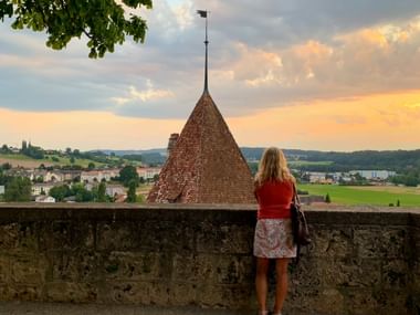 Frau blickt über eine Mauer auf das Schloss Murten bei Sonnenuntergang